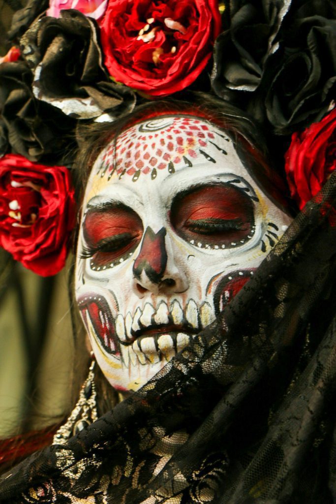 Close-up portrait of a woman with colorful Day of the Dead face paint and floral headdress.