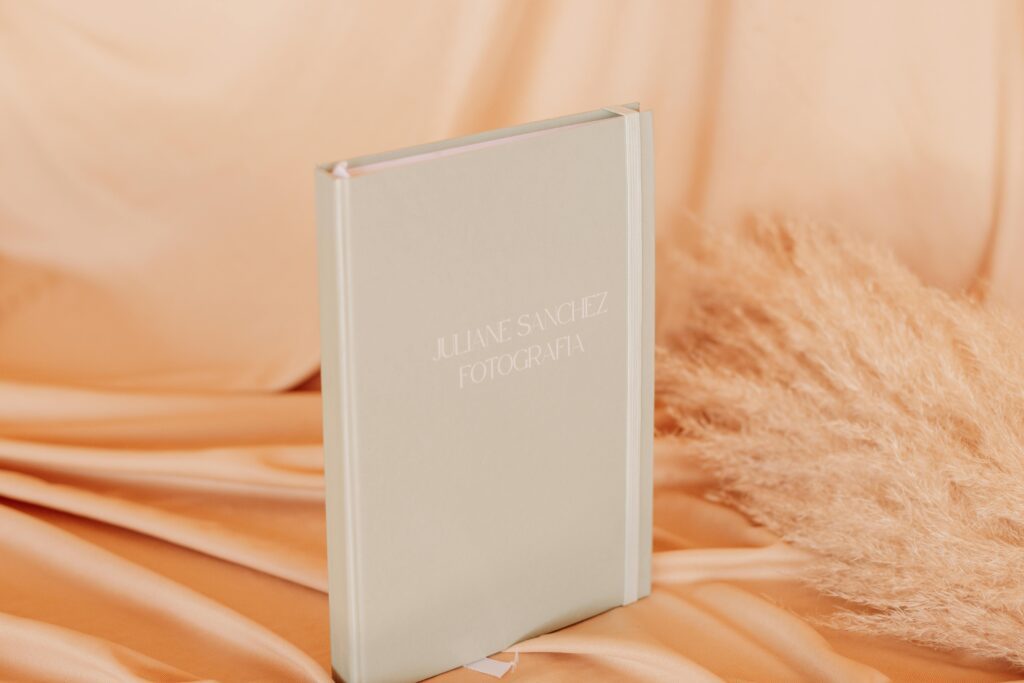 A beautifully designed hardcover photo album set against a soft satin fabric backdrop.