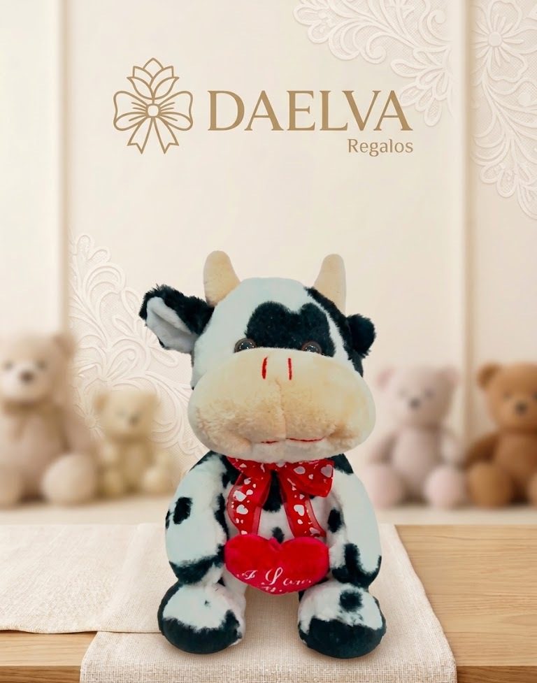 Peluche de vaca blanca y negra con un lazo rojo de corazones y un corazón rojo entre las patas