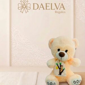 Osito de peluche crema sentado con un babero blanco con dibujo de un árbol y nariz marrón